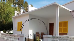 Un edificio blanco con un porche cubierto, una entrada protegida por una reja y contraventanas amarillas.
