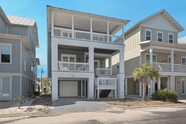 A two-story residential building with a front garage, a balcony on the second floor, and a palm tree in the front yard. - 🌊Dip Your Toes: Pet-Friendly Cottage w/ Intracoastal Access and Community Pool (Navarre)