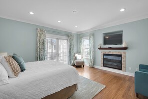 A bedroom with a large bed, a fireplace, a television, and a view of the outside. - 🌊Dip Your Toes: Pet-Friendly Cottage w/ Intracoastal Access and Community Pool (Navarre)