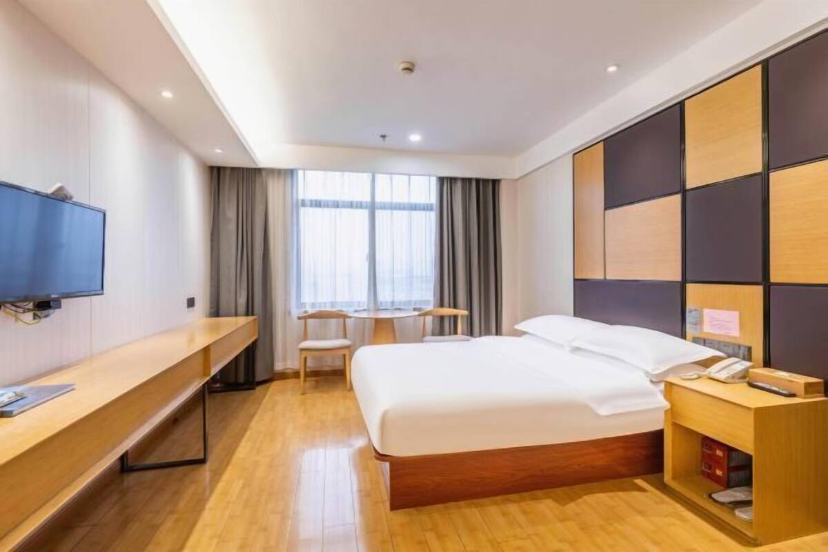A hotel room with a bed, a desk, a TV, a small table, and a window with curtains.