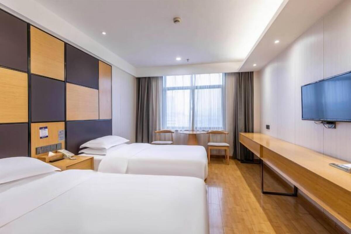 A hotel room with two beds, a desk, a chair, a TV, and a window with curtains.