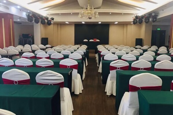 A conference room with rows of tables, white chairs with red sashes, and a stage at the front. - Shucheng Saifu Hotel (Shucheng)