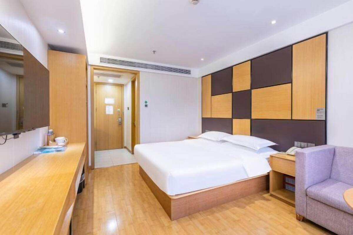 A hotel room with a bed, bedside table, chair, and a TV.