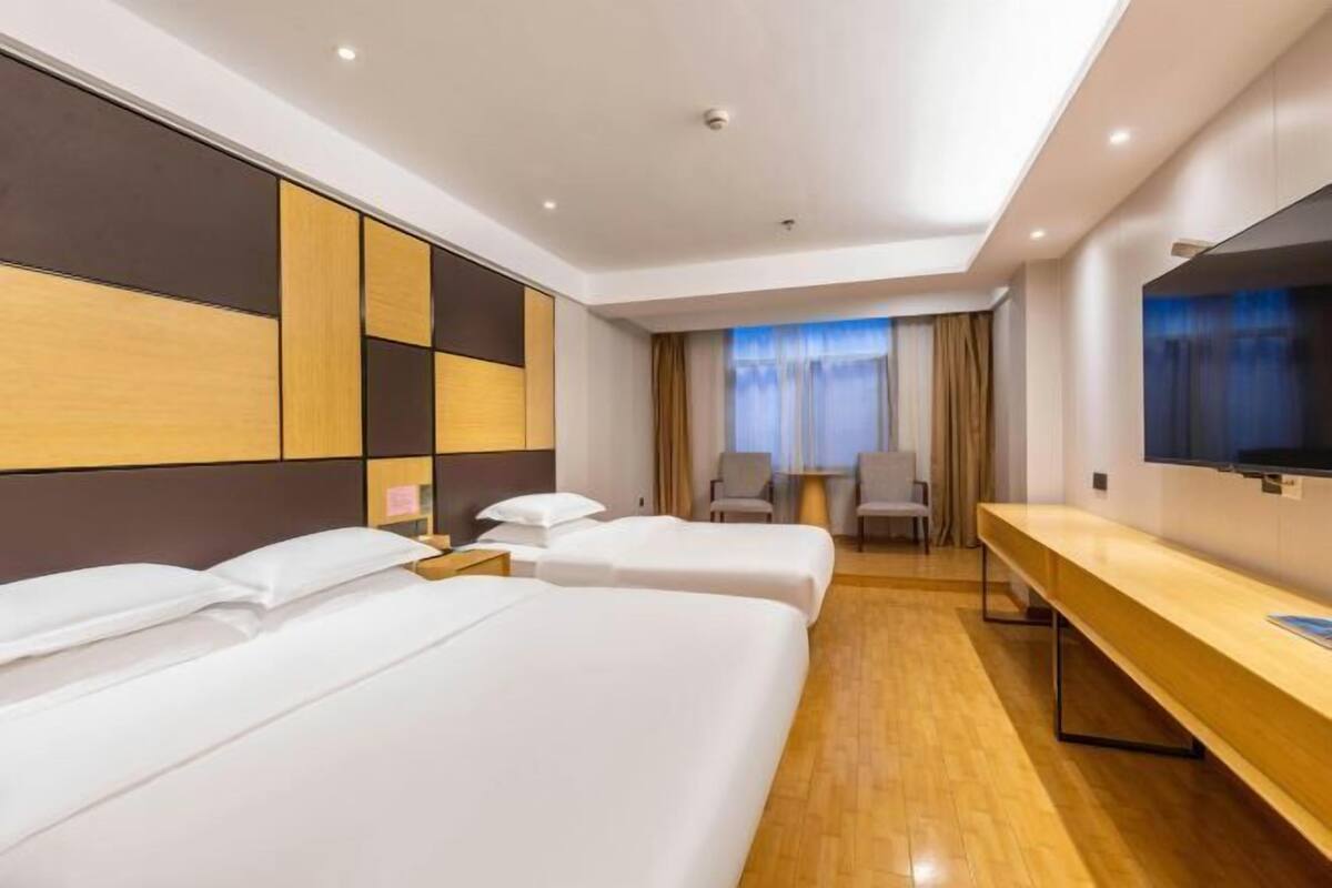 A hotel room with two beds, a wooden desk, a TV, and a window with curtains.