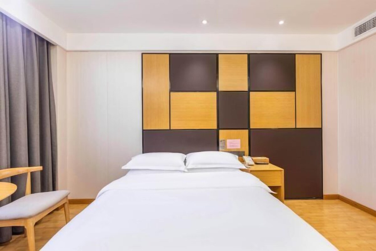 A hotel room with a bed, a bedside table with a phone, a chair, and a curtain.