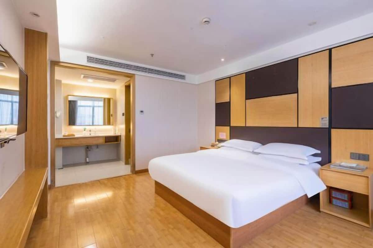 A modern hotel room with a large bed, wooden headboard, bedside tables, and a mirror.