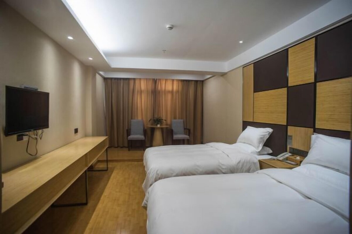 A hotel room with two beds, a desk, a TV, and a small table with chairs.