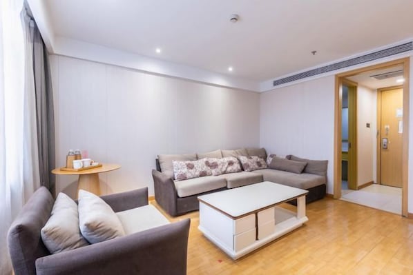 A modern living room with a grey sofa, a white coffee table, and a small round table with a tray of items. - Shucheng Saifu Hotel (Shucheng)