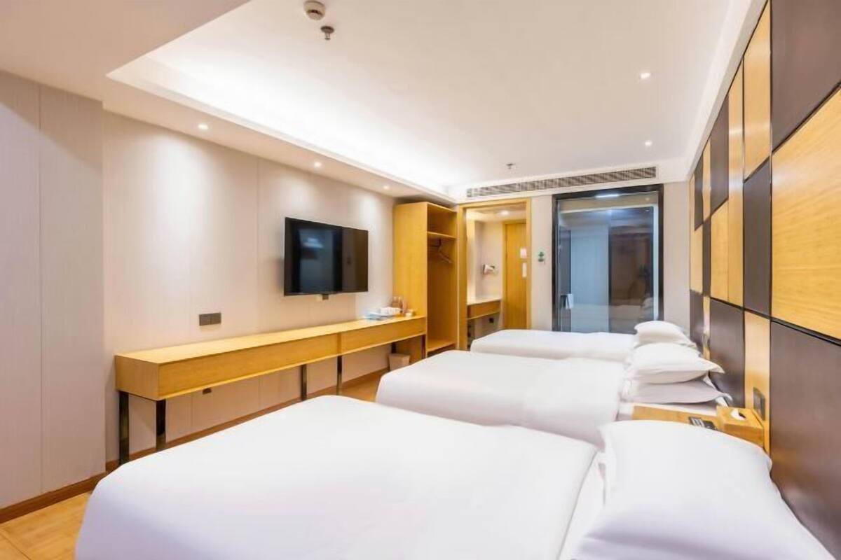 A hotel room with three beds, a TV, a wooden bench, and a wardrobe.