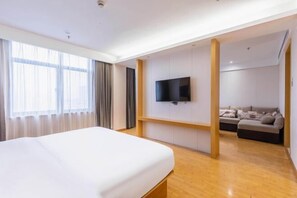 Una habitación de hotel moderna con una cama grande, un televisor en la pared, un sofá y un ventanal con cortinas.