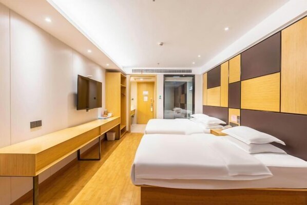 Una habitación de hotel moderna con suelo de madera, un banco largo, dos camas con sábanas blancas, un televisor de pantalla plana y un armario con combinación de madera y paneles oscuros.