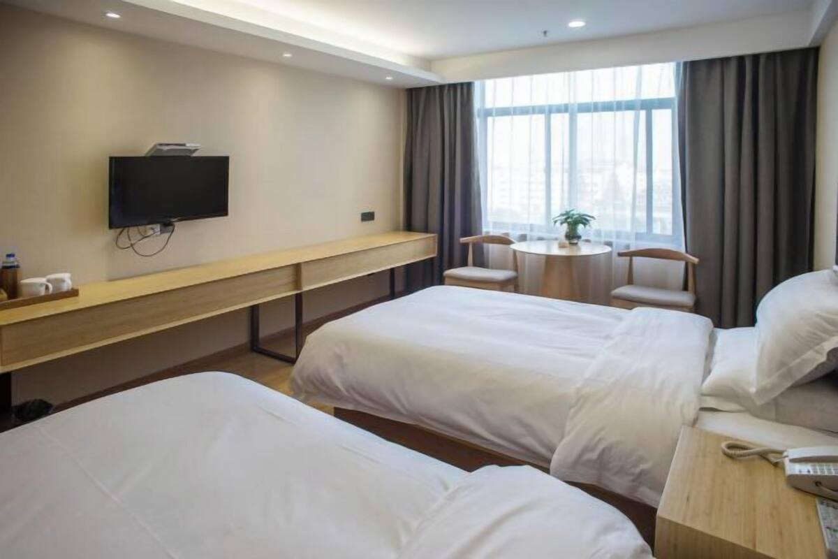 A hotel room with two beds, a TV, a small table, and a window with curtains.