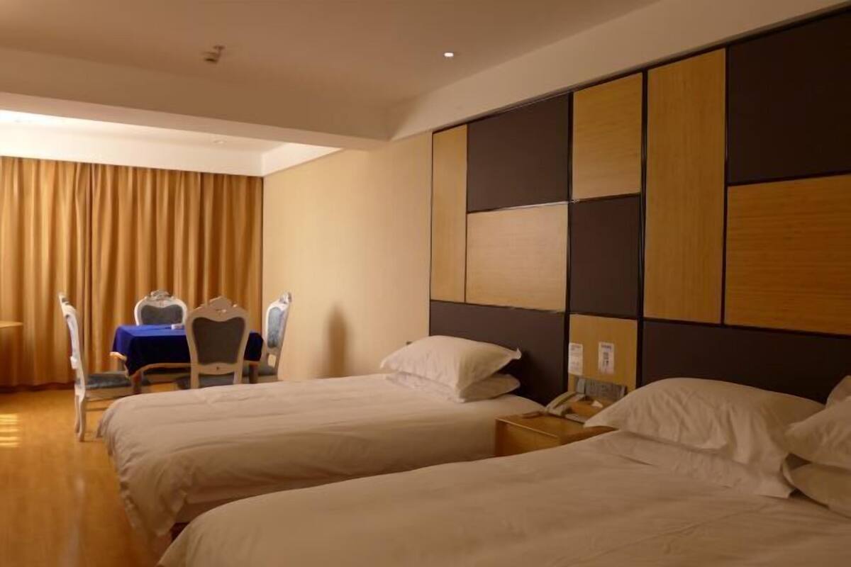 A hotel room with two beds, a desk, a chair, and a view of the outdoors.