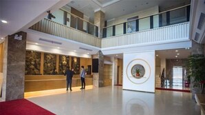Un vestíbulo amplio con alfombra roja, un mostrador de recepción y un elemento decorativo circular en la pared.