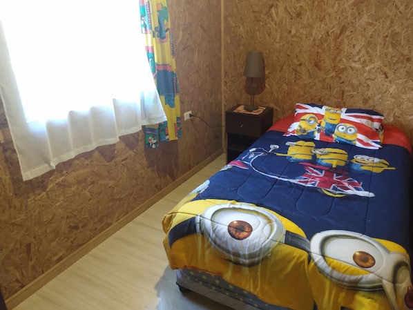Ein Schlafzimmer mit Minion-Bettwäsche, einem Fenster mit Vorhängen und einem Nachttisch mit Lampe.