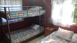 A dormitory room with bunk beds, a bedside table with a lamp, and a window with curtains.