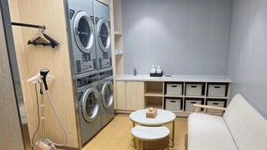 A compact room with a washing machine, a vacuum cleaner, a small round table, a sofa, and storage boxes. - Ji Hotel (Hangzhou)