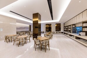 A modern dining area with multiple tables and chairs, a central column, and a kitchen area with shelves. - Ji Hotel (Hangzhou)