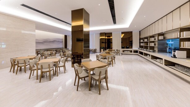 A modern dining area with multiple tables and chairs, a central column, and a kitchen area with shelves. - Ji Hotel (Hangzhou)