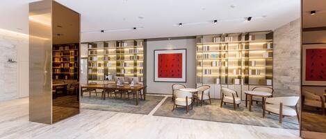 A modern library with bookshelves, a dining area with tables and chairs, and a large red artwork on the wall.
