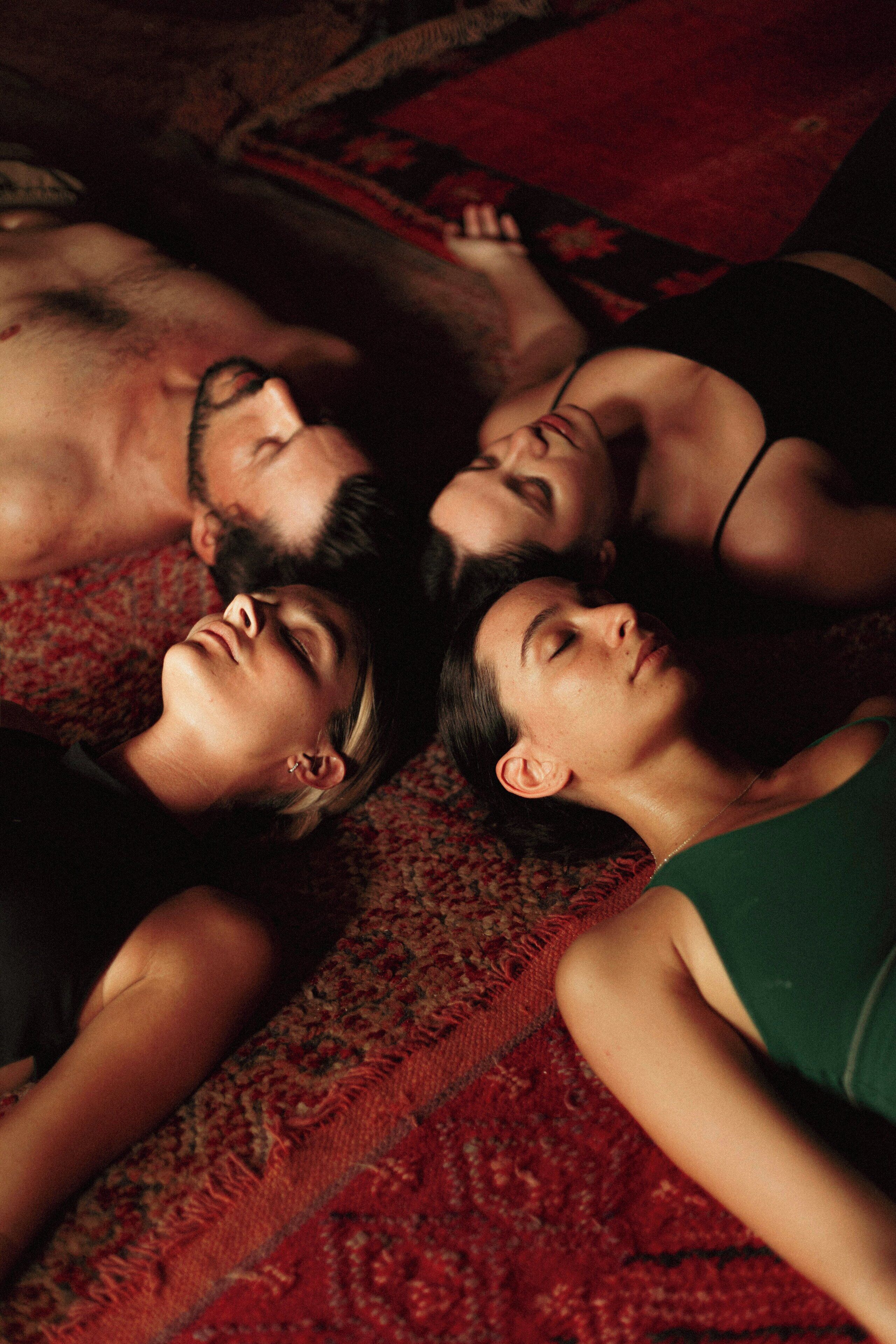 Three people lying on a patterned carpet.