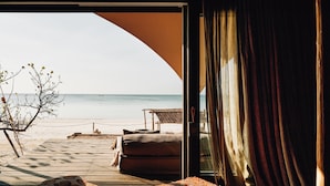 A beach view from a room with a wooden deck, a sofa, and a rug. - Nômade Temple Holbox (Isla Holbox)