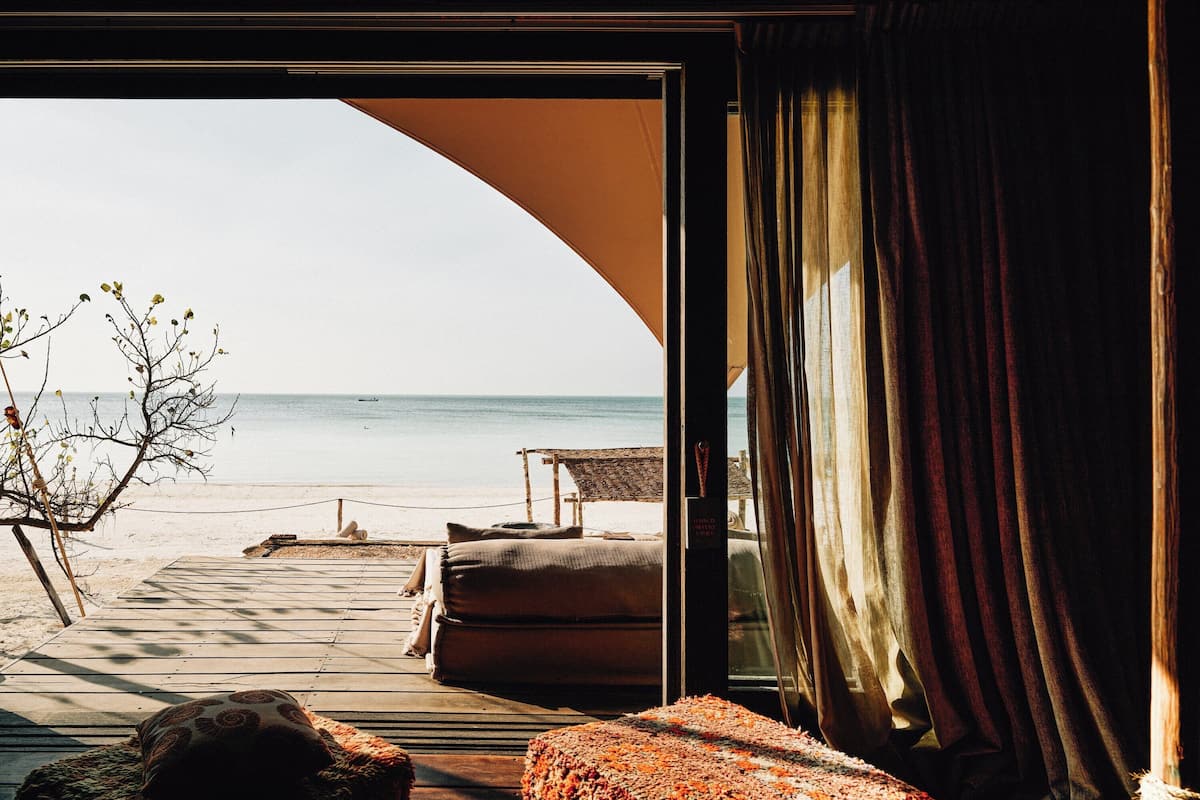 Vista a la playa desde una habitación con terraza de madera, un sofá y una alfombra.