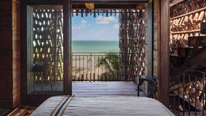 A room with a wooden floor, a bed, a balcony with a view of the beach and ocean, and a wooden bookshelf. - Nômade Temple Holbox (Isla Holbox)