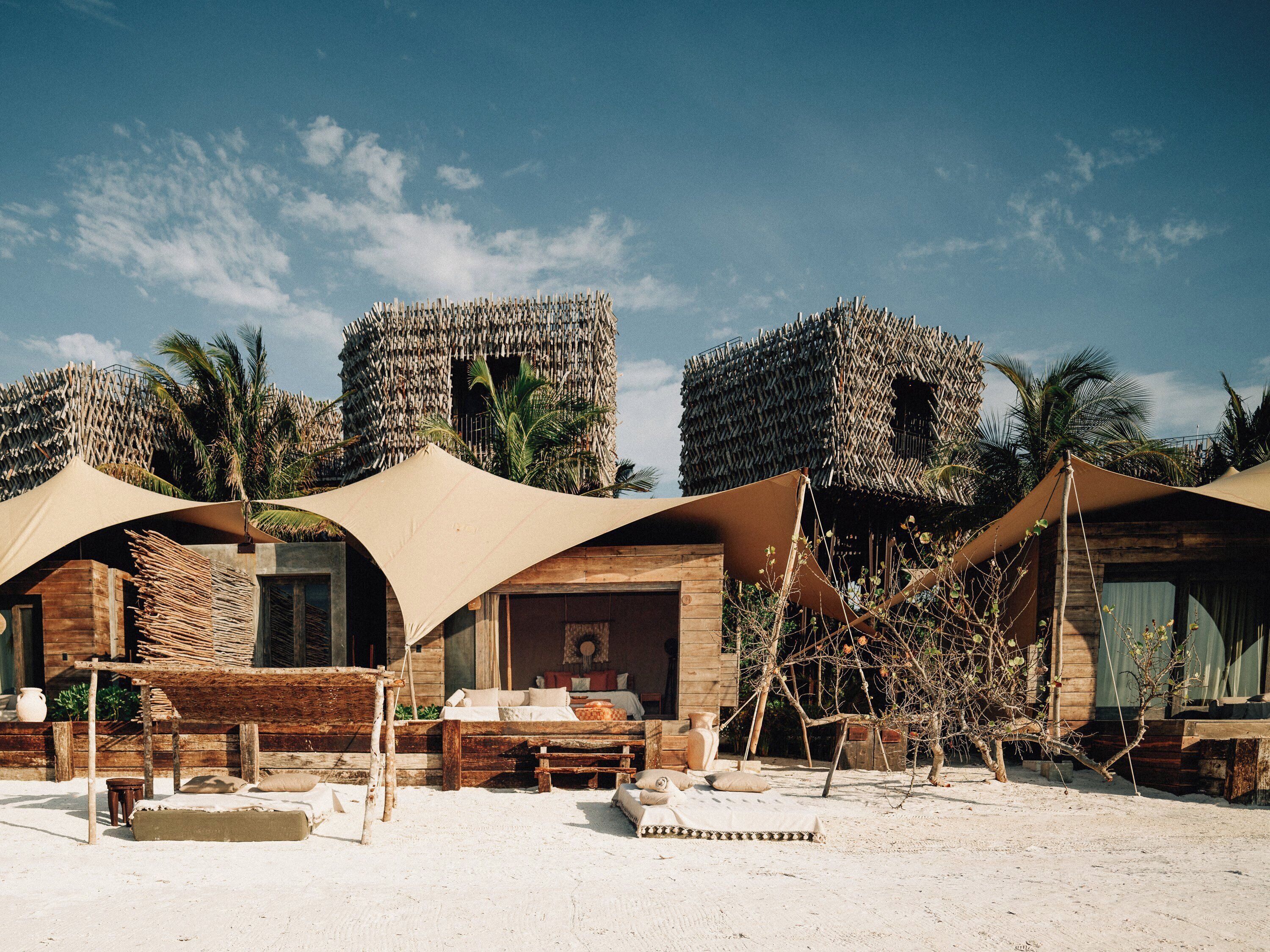 Een woestijnhotel met rieten hutten, zand en palmbomen.