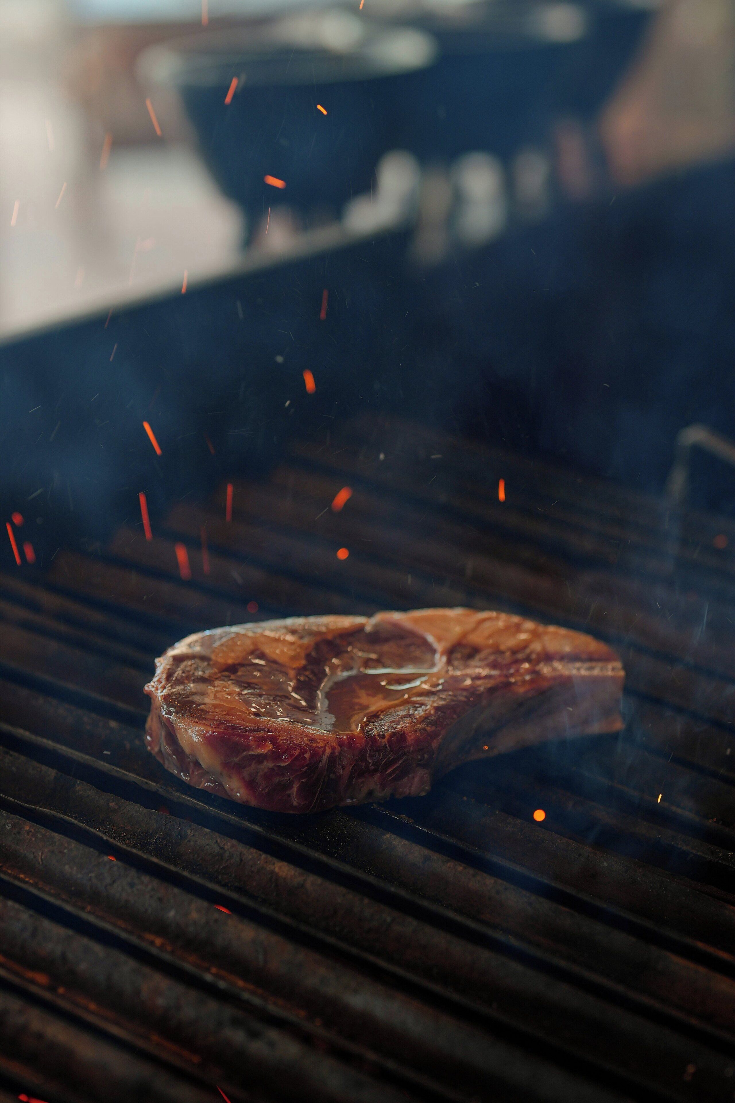 A steak grilling on a grill with visible sparks.