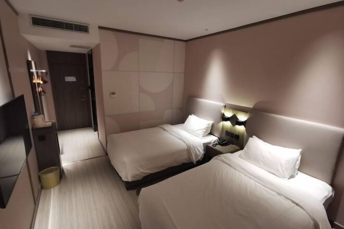 A hotel room with two beds, a TV, a bedside table, and a wall-mounted lamp.