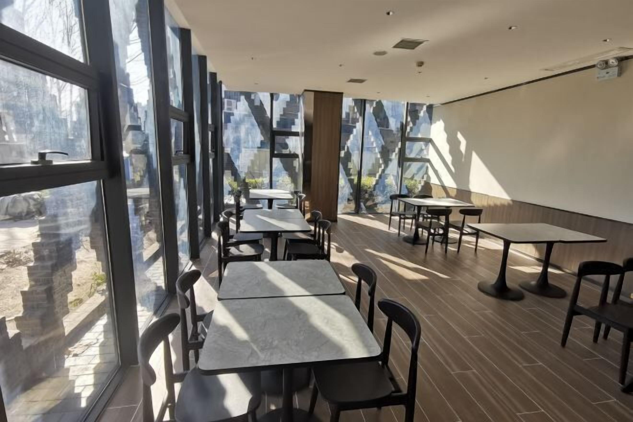 A modern restaurant with large windows, tables, and chairs arranged for dining.