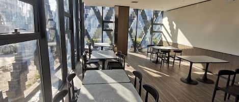 A modern restaurant with large windows, tables, and chairs arranged for dining.