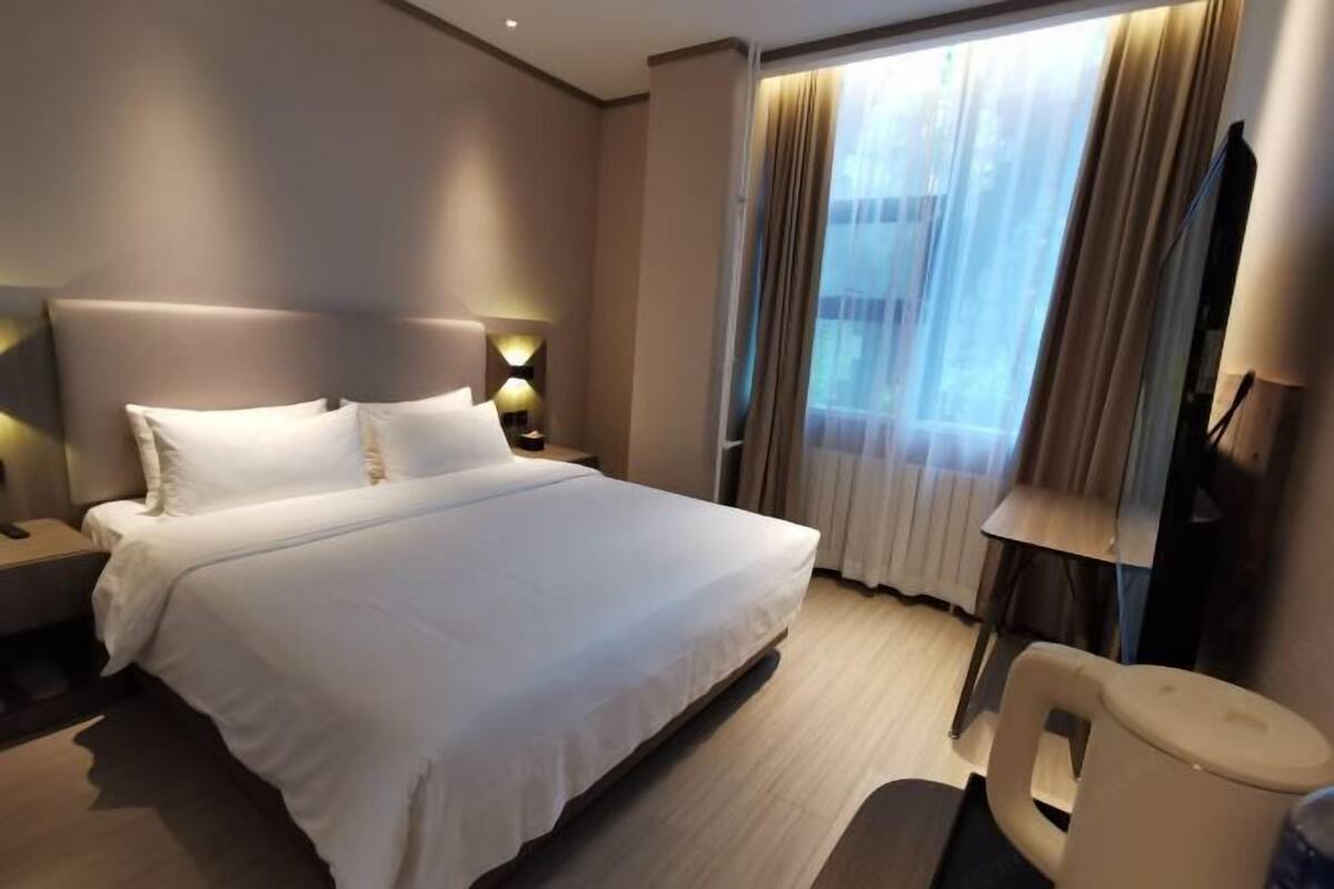 A hotel room with a large bed, bedside lamps, a TV, and a window with curtains.