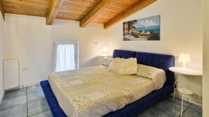 A bedroom with a wooden ceiling, a bed with a blue headboard, two bedside lamps, and a painting on the wall. - St. Francis apartment (Agropoli)
