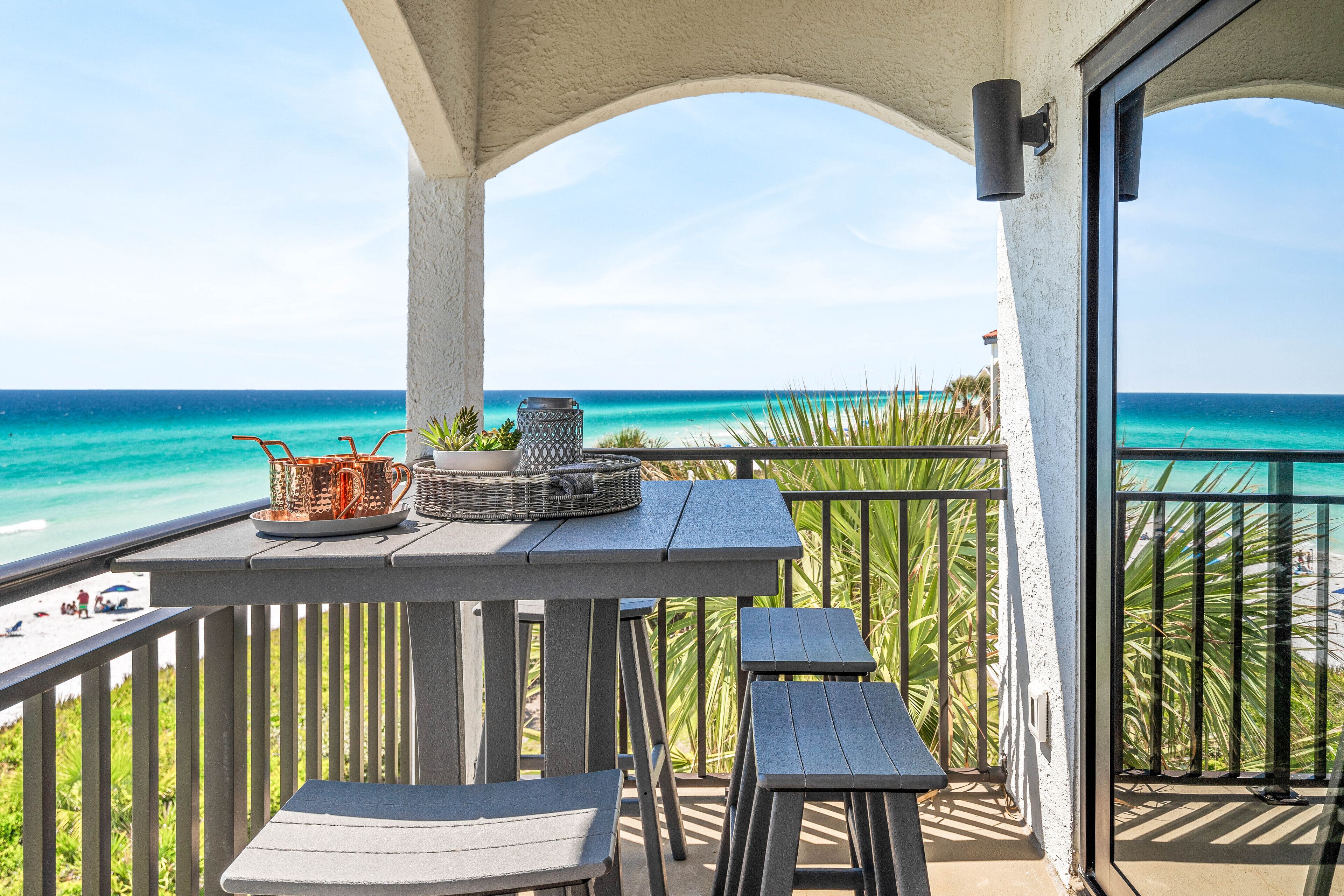Un balcon avec vue sur l’océan, une table avec un panier et une tasse, et deux chaises.