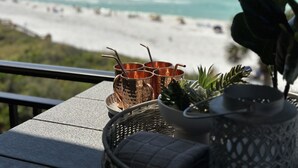 A terrace with a view of the beach, featuring a table with copper mugs and a potted plant. - GORGEOUSLY RENOVATED! Palms C15, Gulf-Front,CORNER-UNIT, MODERN & FACING SUNSET! (Santa Rosa Beach)