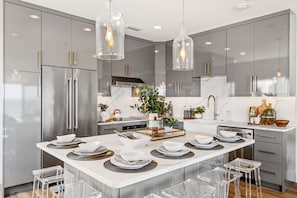 A modern kitchen with stainless steel appliances, a marble countertop, and clear glass pendant lights.