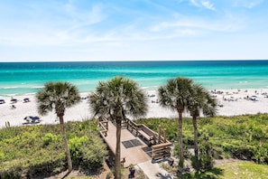 A beach with a wooden deck, palm trees, and a view of the ocean.