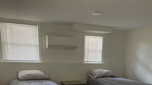 Une chambre avec deux lits, une petite table de chevet et un climatiseur fixé au mur.