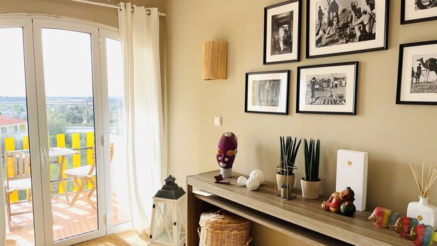 A room with a sliding glass door leading to a balcony, a wooden shelf with decorative items, and framed black and white photographs on the wall. - Boho Tavira Apartment (Tavira)