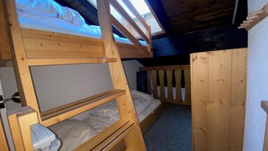 Een slaapkamer met stapelbed, dakraam, houten wanden en een deur.
