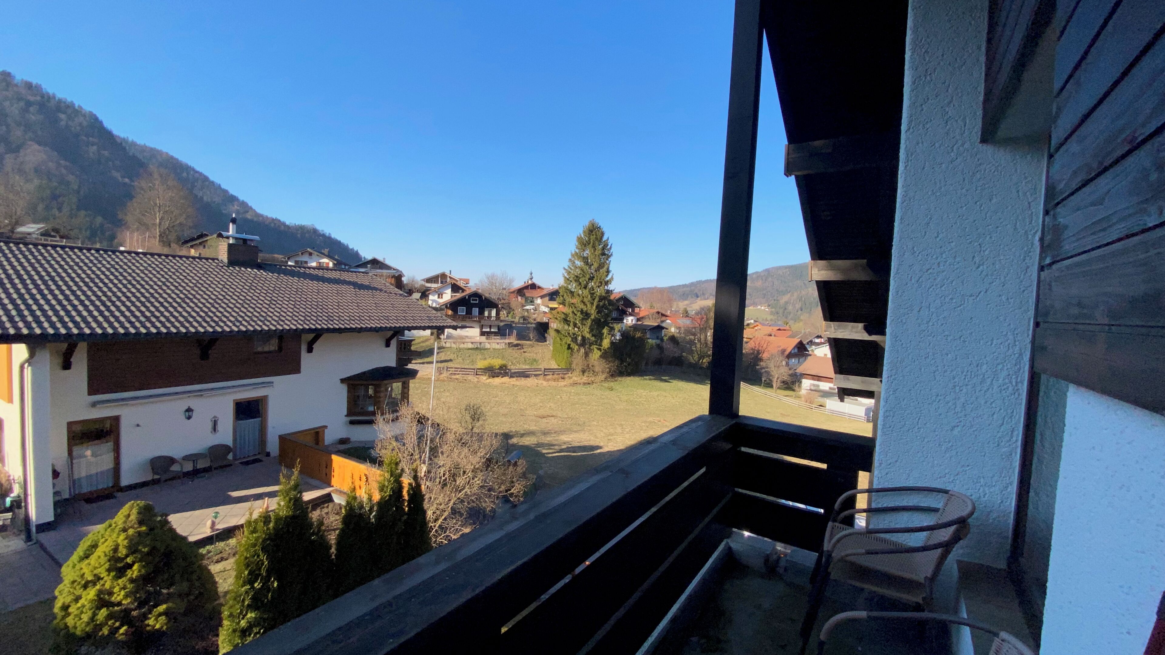 Ein Balkon mit Blick auf ein Dorf, ein Berg im Hintergrund und ein klarer Himmel.