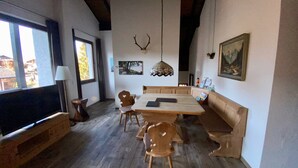 Een eetgedeelte met een houten tafel, stoelen, een televisie en een kroonluchter.