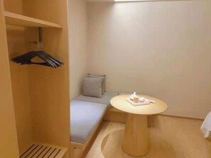 A small, compact room with a bed, a bedside table, a hanging coat rack, and a single pillow. - Ji Hotel (Wuhan)