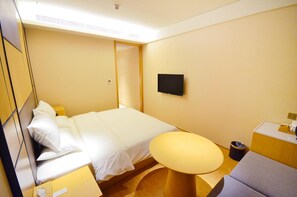 A hotel room with a bed, a small round table, a TV mounted on the wall, and a trash bin. - Ji Hotel (Wuhan)