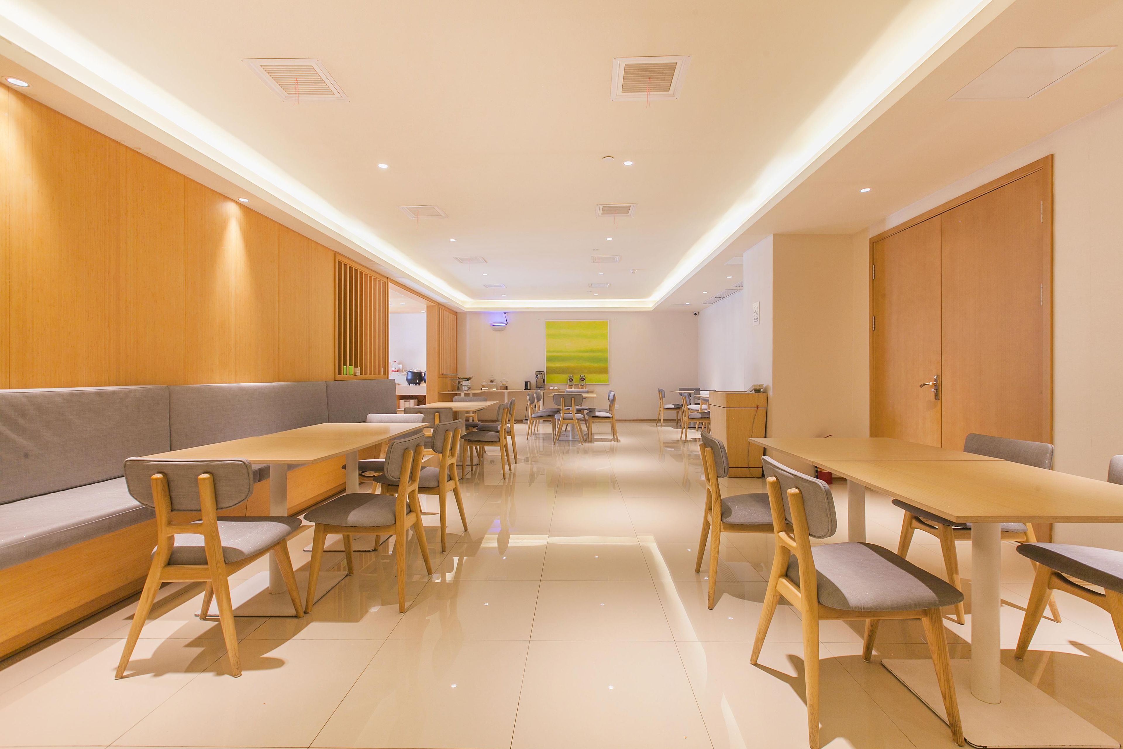 A modern dining area with wooden furniture, recessed ceiling lights, and a large window with a view.