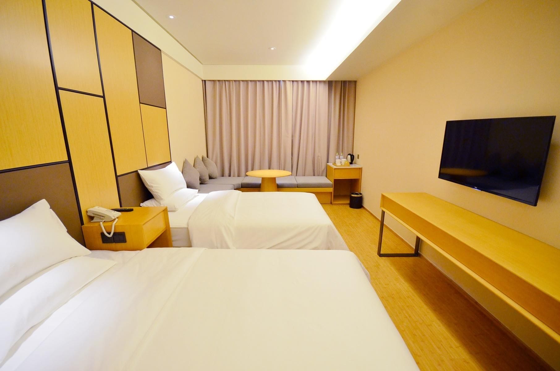 A hotel room with two beds, a desk, a television, and a window with curtains.