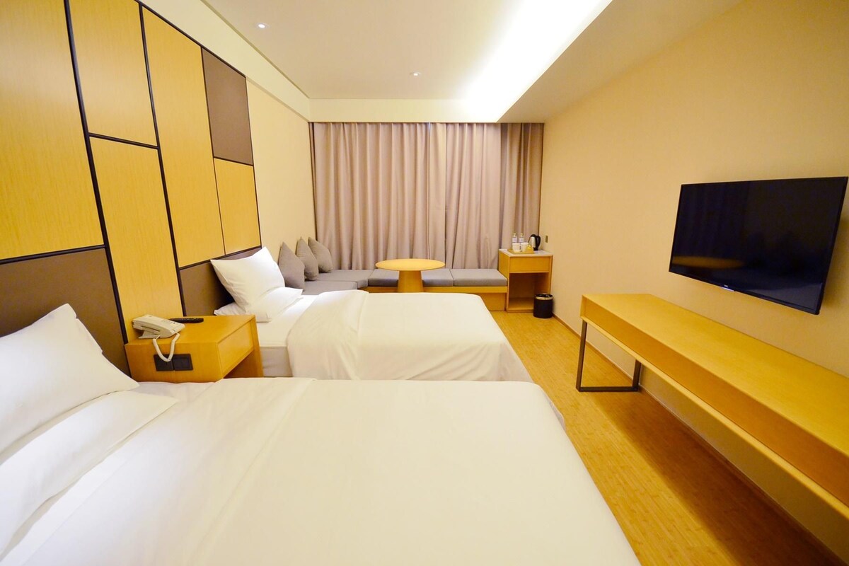 Une chambre d’hôtel avec deux lits, un bureau, une télévision et une fenêtre avec des rideaux.