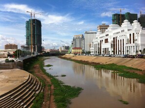 A river with a bridge, a white building with columns, and a construction crane in the background. - Ofuro Hotel (Phnom Penh)